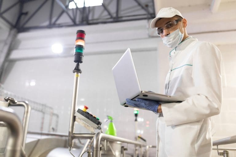 Portrait of man in a white robe and a cap standing in production department of dairy factory with