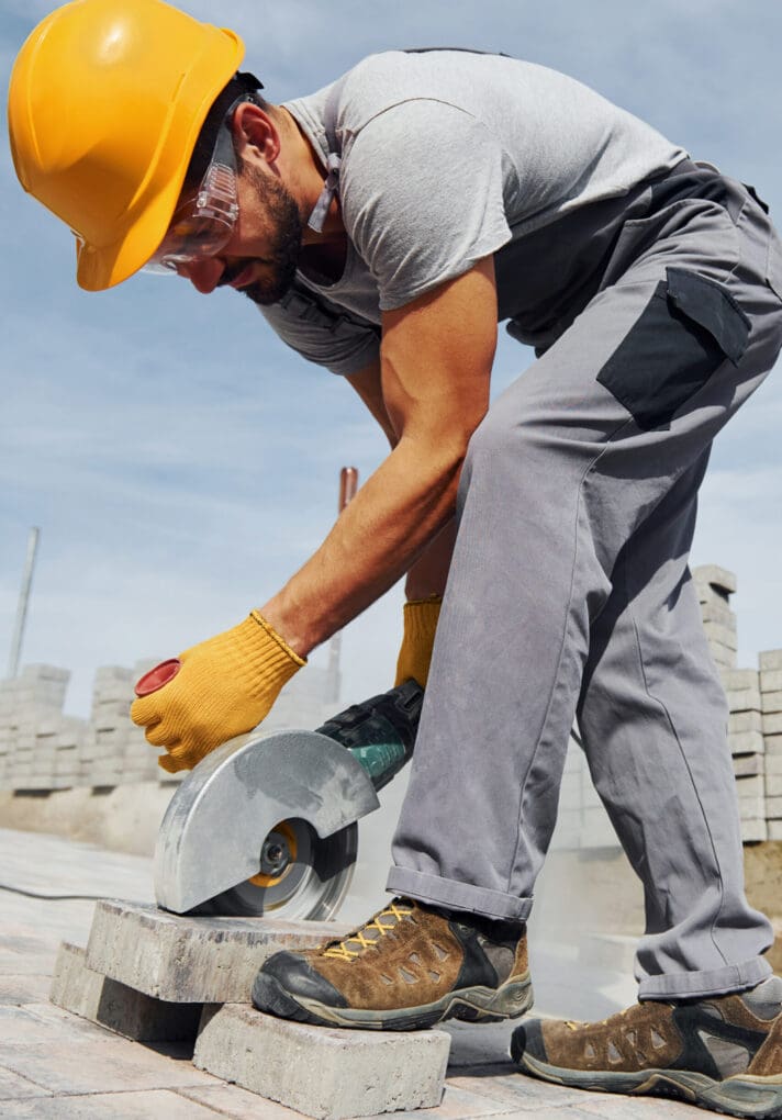 Uses circular saw. Male worker in yellow colored uniform have job with pavement.